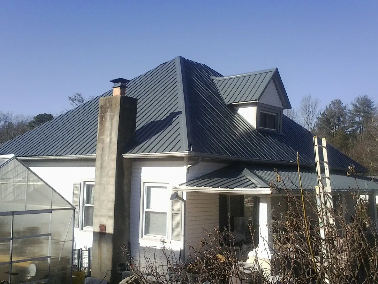 Dark blue standing seam metal roof on a white farmhouse with dormer — Slate & Tile Roof Repair by Roofing Brothers in Coon Rapids