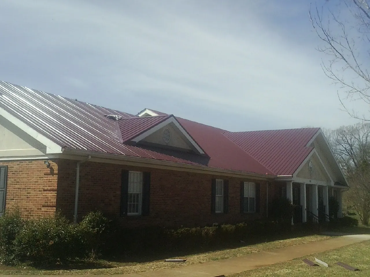 Red metal roof with gabled entries on a long brick building, from a Hail Damage Roof Repair job in Coon Rapids