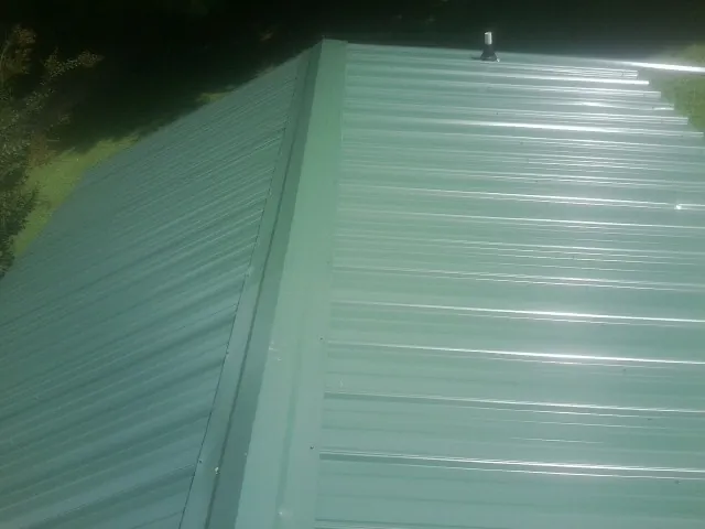 New green metal panels meeting at the ridge of a roof — Flat Roof Repair work by our crew in Coon Rapids