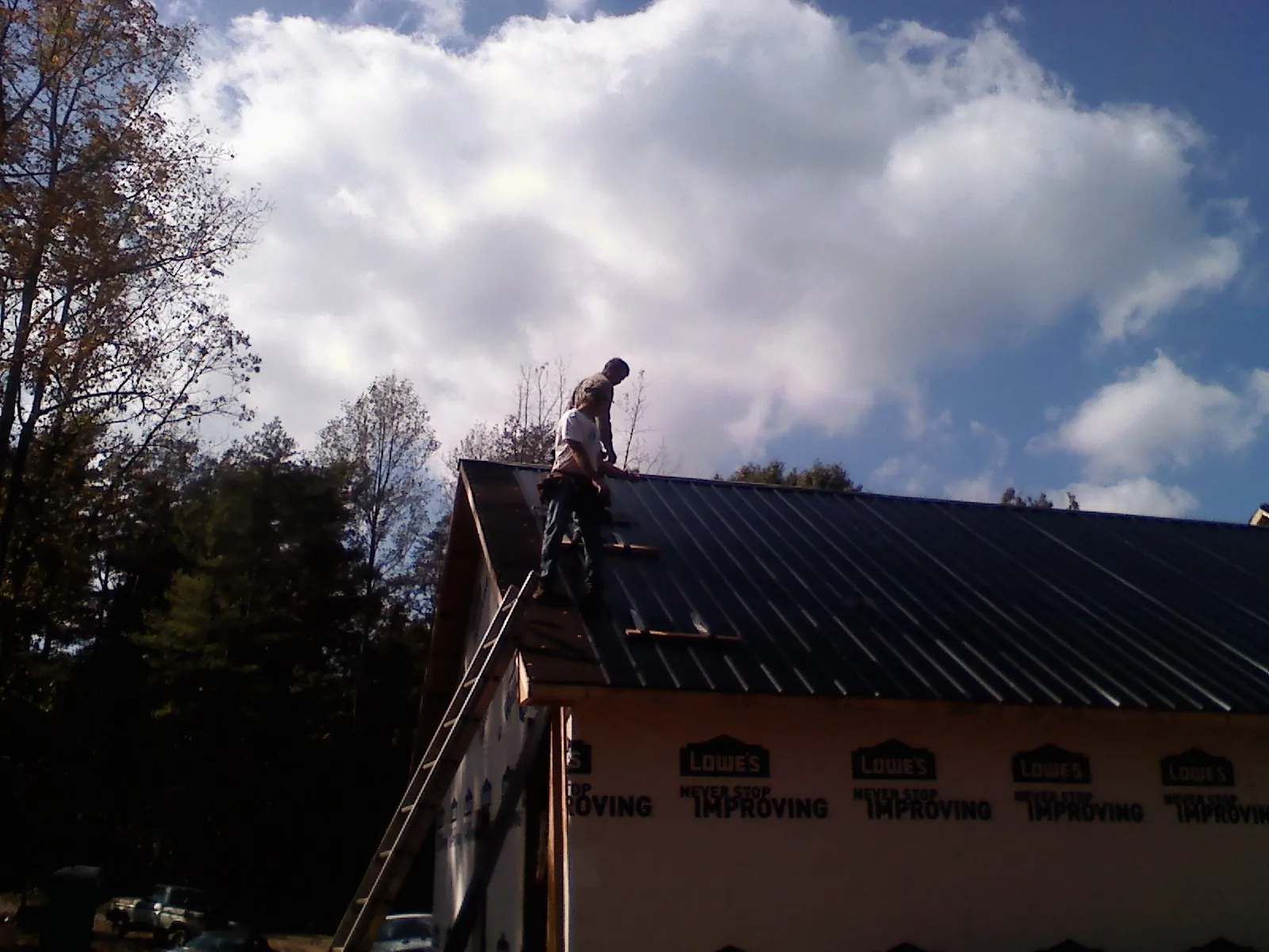 Roofer fastening dark metal panels high against a cloudy sky, from a Roof Inspection job in Coon Rapids