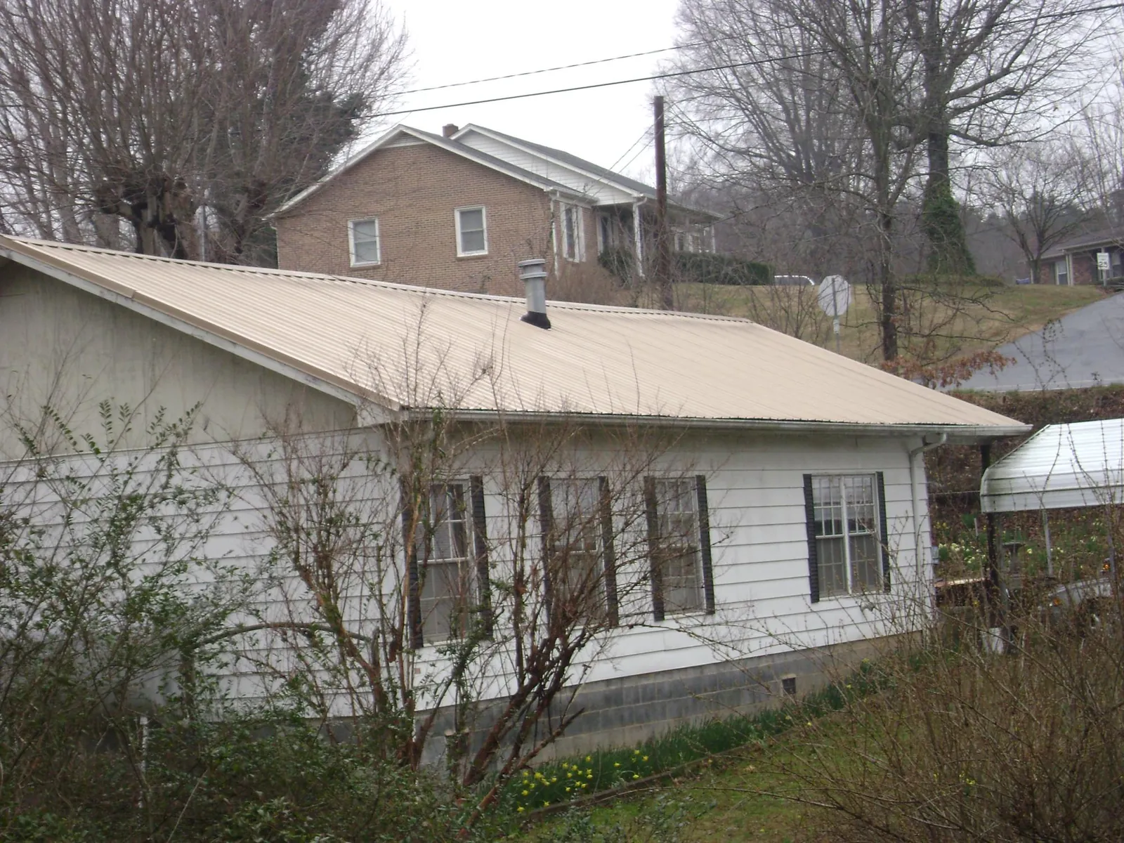Tan metal roof on a white sided house set into a hillside — Commercial Roofing by Roofing Brothers in Coon Rapids