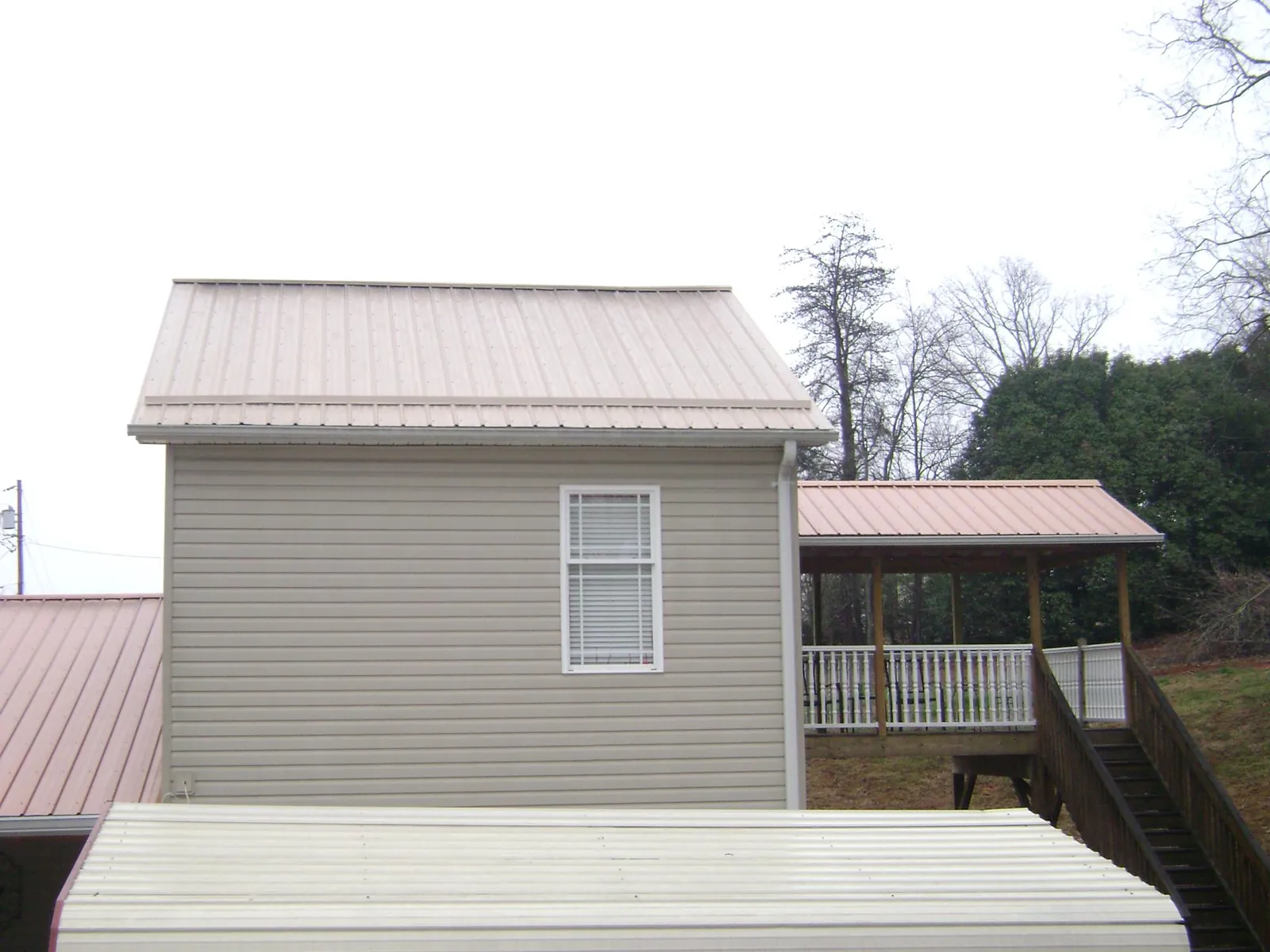 Tan metal roofs on a two story addition and attached porch, from a Roof Replacement job in Coon Rapids
